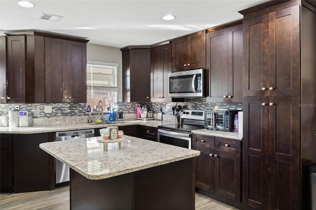 kitchen with light stone counters, a kitchen island, light wood-type flooring, appliances with stainless steel finishes, and sink