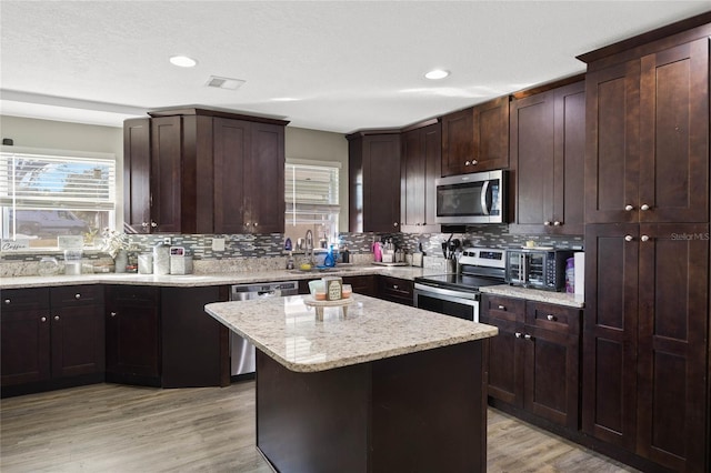 kitchen with light stone counters, a center island, light hardwood / wood-style floors, decorative backsplash, and appliances with stainless steel finishes