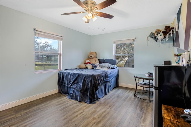 bedroom with wood-type flooring, ceiling fan, and stainless steel fridge