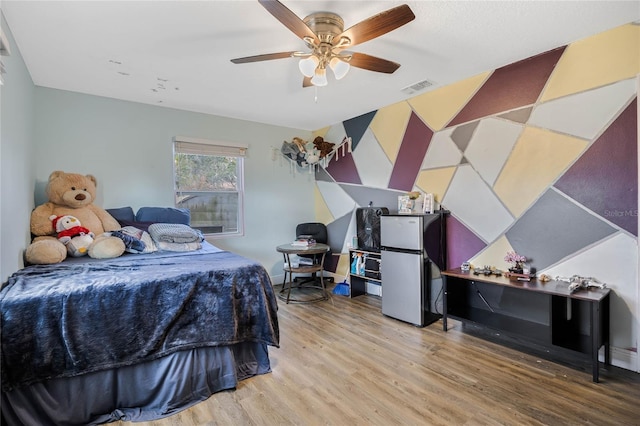 bedroom featuring wood-type flooring, ceiling fan, and stainless steel fridge