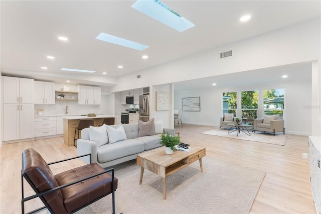 living room with sink, a skylight, and light hardwood / wood-style flooring