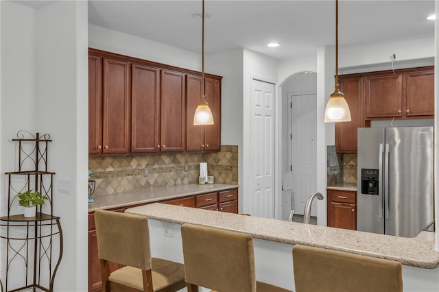 kitchen featuring a kitchen breakfast bar, backsplash, stainless steel fridge with ice dispenser, and hanging light fixtures