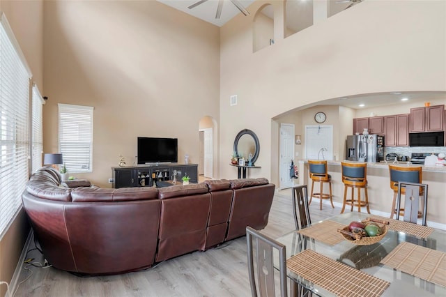 living room with ceiling fan, light hardwood / wood-style flooring, a towering ceiling, and sink