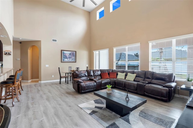 living room with a towering ceiling, ceiling fan, and light hardwood / wood-style flooring