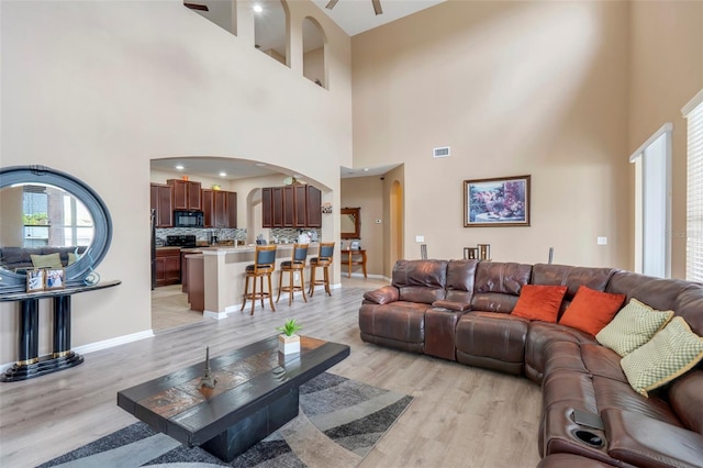 living room featuring ceiling fan, light wood-type flooring, and a towering ceiling