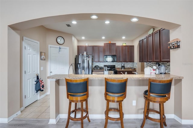 kitchen with a breakfast bar area, black appliances, kitchen peninsula, light tile patterned floors, and decorative backsplash