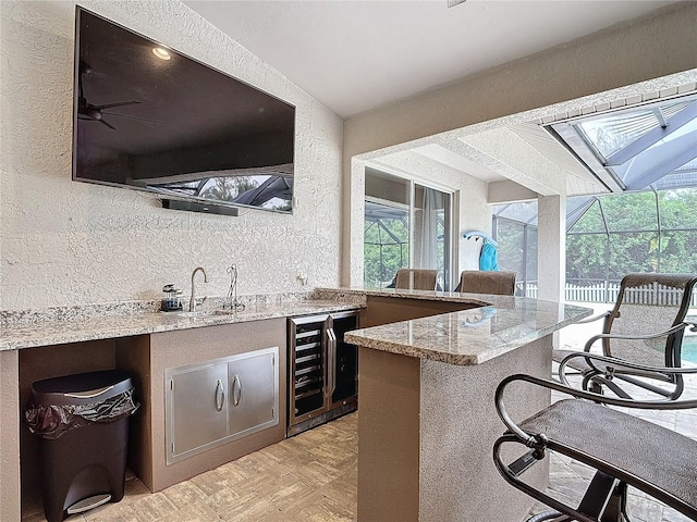 bar with wine cooler, light parquet flooring, ceiling fan, sink, and light stone counters