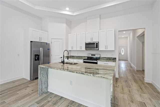 kitchen featuring light stone countertops, a center island with sink, white cabinets, appliances with stainless steel finishes, and sink