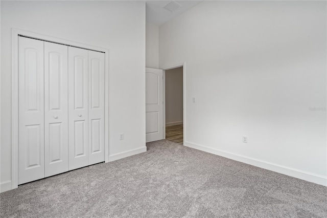 unfurnished bedroom featuring a towering ceiling, a closet, and carpet