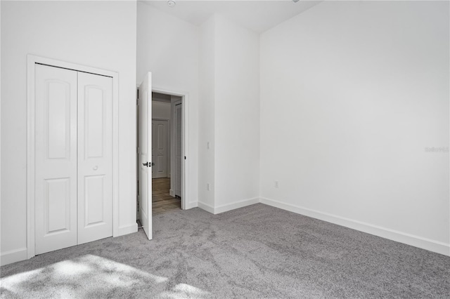 unfurnished bedroom with a high ceiling, a closet, and light carpet