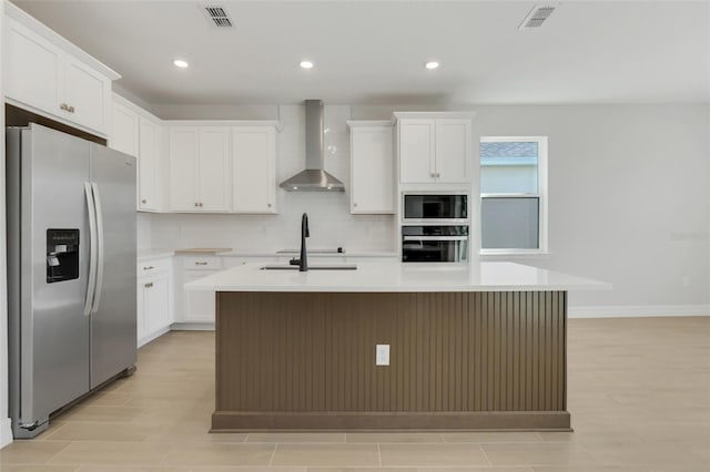 kitchen featuring wall chimney range hood, stainless steel refrigerator with ice dispenser, an island with sink, white cabinets, and black oven