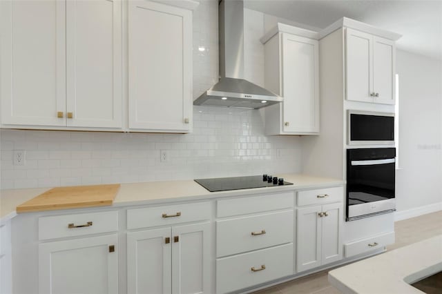 kitchen with white cabinets, light countertops, wall chimney range hood, backsplash, and black appliances