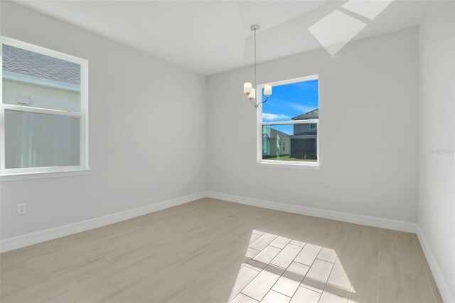 empty room featuring a chandelier, baseboards, and light wood finished floors