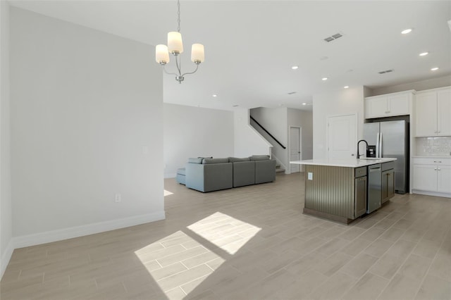 kitchen with white cabinets, an island with sink, appliances with stainless steel finishes, open floor plan, and light countertops