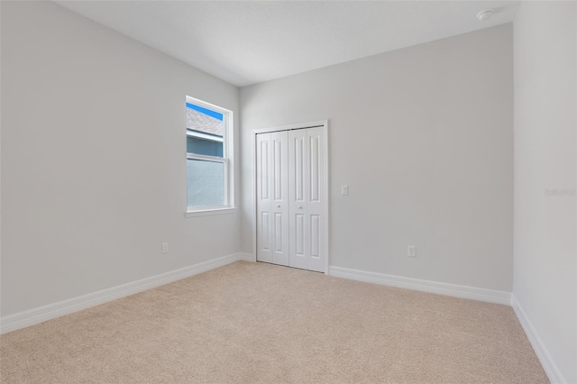 unfurnished bedroom with baseboards, a closet, and light colored carpet