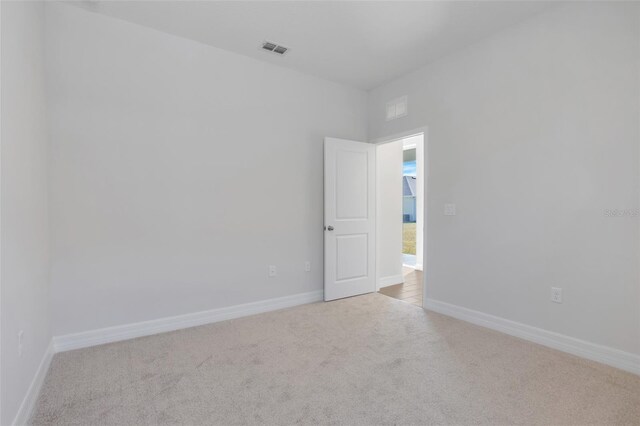 spare room featuring baseboards, visible vents, and light colored carpet