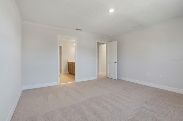 unfurnished bedroom featuring a textured ceiling, connected bathroom, light carpet, visible vents, and baseboards