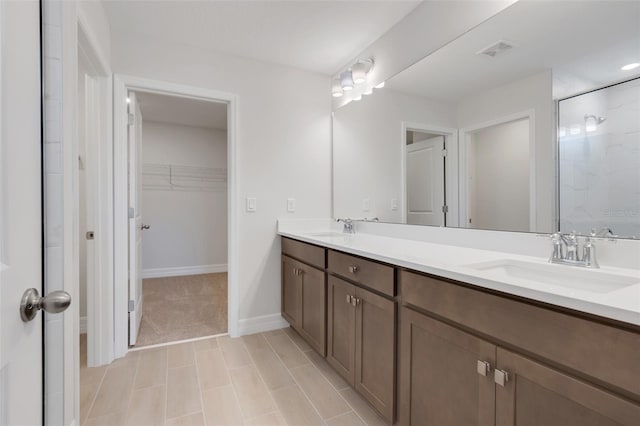 full bath with double vanity, visible vents, a walk in closet, and a sink