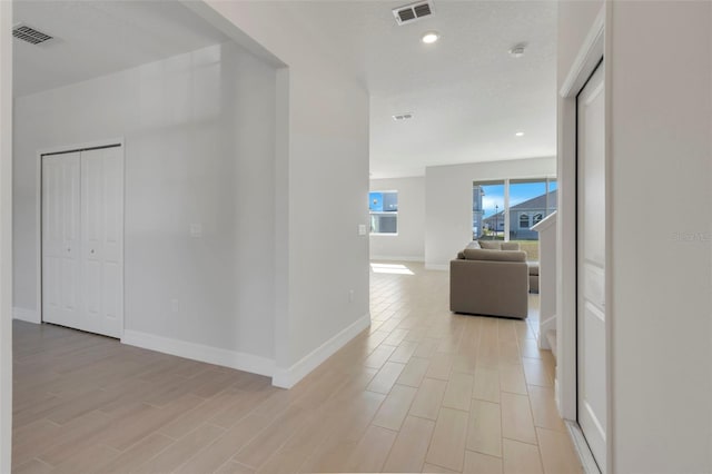 hallway with light wood-type flooring, visible vents, and baseboards