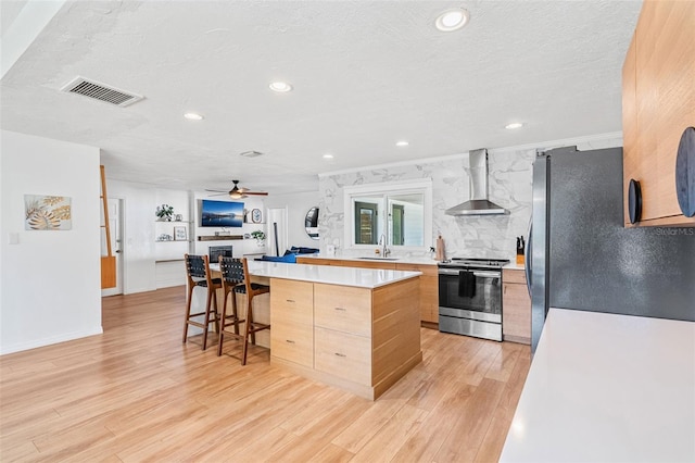 kitchen with wall chimney exhaust hood, stainless steel appliances, a kitchen bar, a kitchen island, and sink