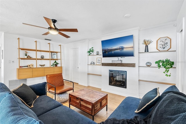 living room featuring ceiling fan, light wood-type flooring, crown molding, and a textured ceiling