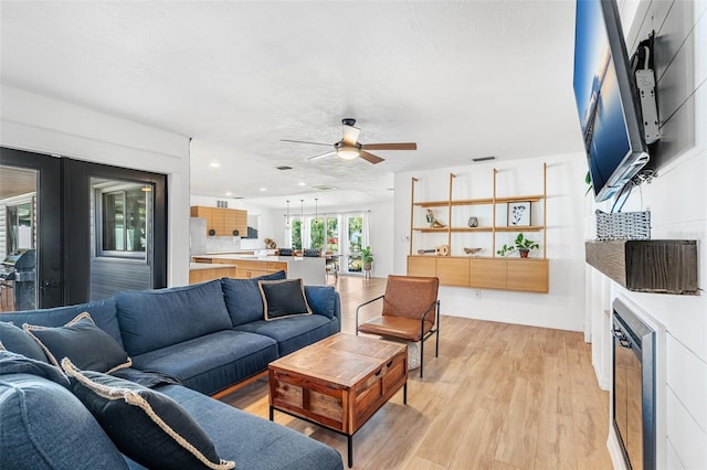 living room featuring ceiling fan, light wood-type flooring, and a textured ceiling