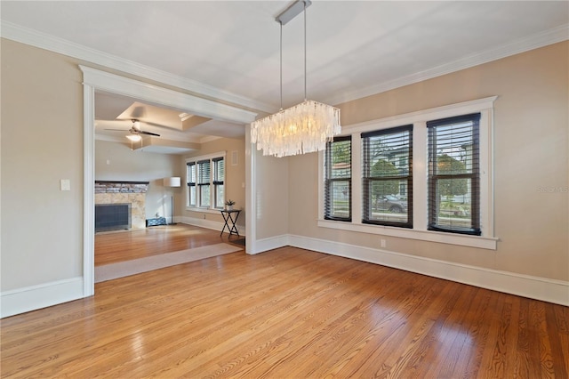 unfurnished dining area with a fireplace, ceiling fan with notable chandelier, ornamental molding, and hardwood / wood-style flooring