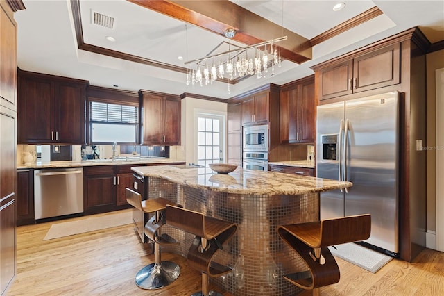 kitchen featuring pendant lighting, appliances with stainless steel finishes, a center island, a tray ceiling, and crown molding