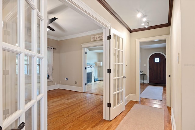 corridor featuring light wood-type flooring, a wealth of natural light, and ornamental molding