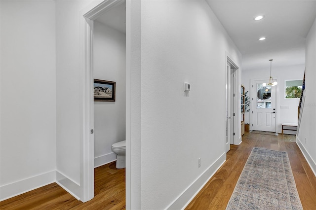 hallway featuring wood-type flooring and an inviting chandelier