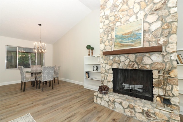 dining area with hardwood / wood-style floors, a chandelier, vaulted ceiling, and a stone fireplace