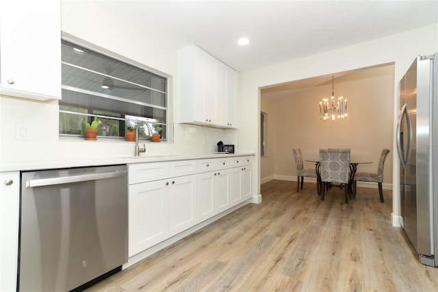 kitchen with stainless steel appliances, white cabinetry, hanging light fixtures, and light hardwood / wood-style flooring