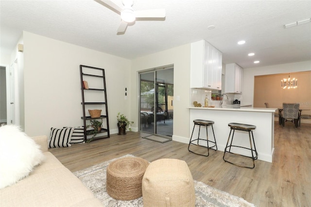 living room with sink, light hardwood / wood-style flooring, a textured ceiling, and ceiling fan with notable chandelier