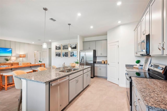 kitchen featuring a kitchen island with sink, stainless steel appliances, light stone counters, sink, and decorative light fixtures