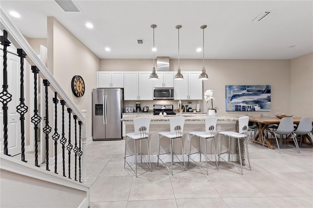 kitchen featuring white cabinetry, hanging light fixtures, a kitchen island with sink, and appliances with stainless steel finishes