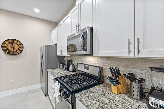 kitchen with dark stone counters, decorative backsplash, white cabinets, stainless steel appliances, and light tile patterned flooring