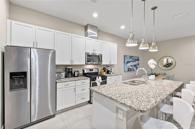 kitchen featuring appliances with stainless steel finishes, decorative light fixtures, white cabinetry, sink, and a kitchen island with sink