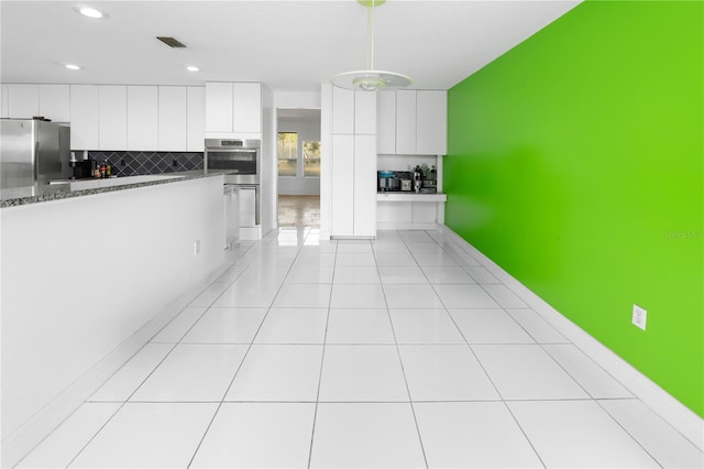 kitchen featuring white cabinets, light tile patterned floors, backsplash, pendant lighting, and appliances with stainless steel finishes