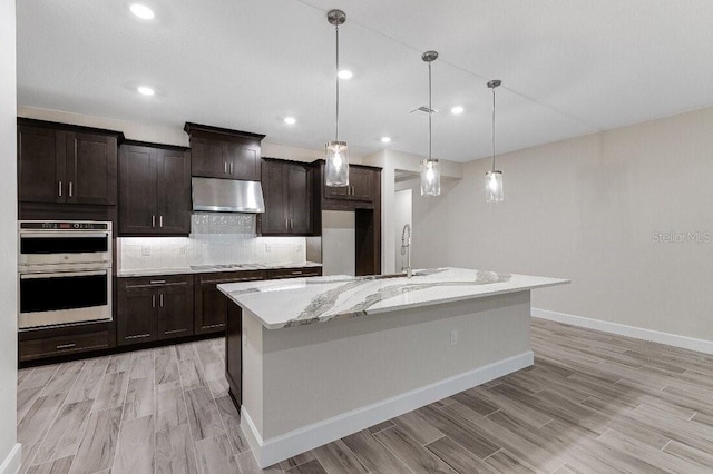 kitchen featuring tasteful backsplash, decorative light fixtures, stainless steel appliances, and an island with sink