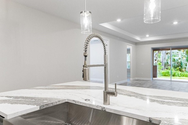 interior details featuring a raised ceiling, hanging light fixtures, sink, and light stone counters