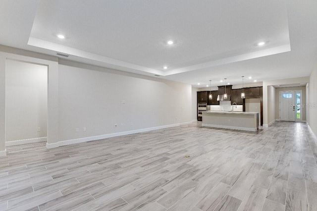 unfurnished living room featuring a tray ceiling, sink, and light wood-type flooring