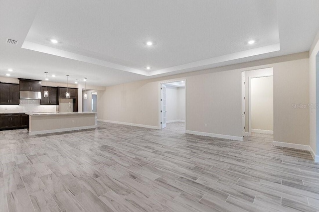 unfurnished living room featuring a raised ceiling and light hardwood / wood-style floors