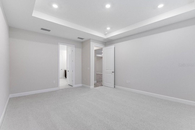 unfurnished bedroom featuring light colored carpet and a raised ceiling