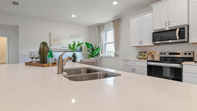 kitchen with backsplash, stainless steel appliances, white cabinets, and sink