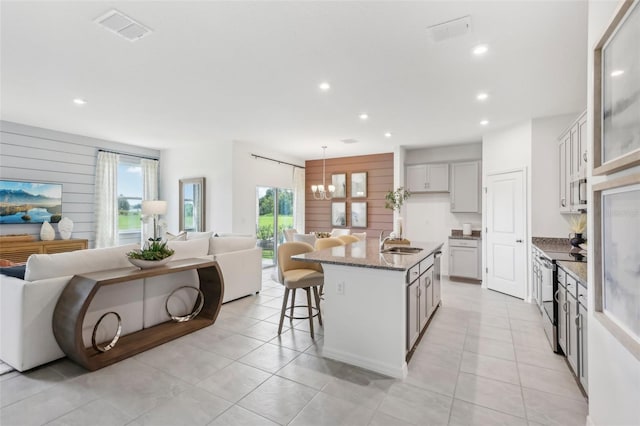 kitchen featuring a kitchen island with sink, stainless steel electric stove, dark stone counters, a kitchen bar, and sink