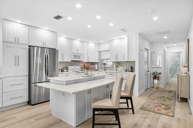 kitchen with white cabinetry, white appliances, a kitchen bar, and a center island