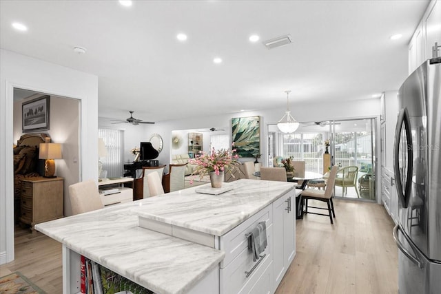 kitchen featuring pendant lighting, stainless steel refrigerator, a center island, light stone counters, and white cabinets