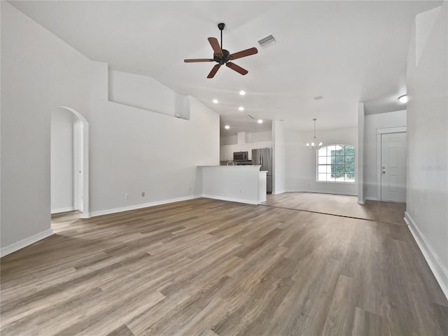 unfurnished living room with ceiling fan with notable chandelier, vaulted ceiling, and wood-type flooring