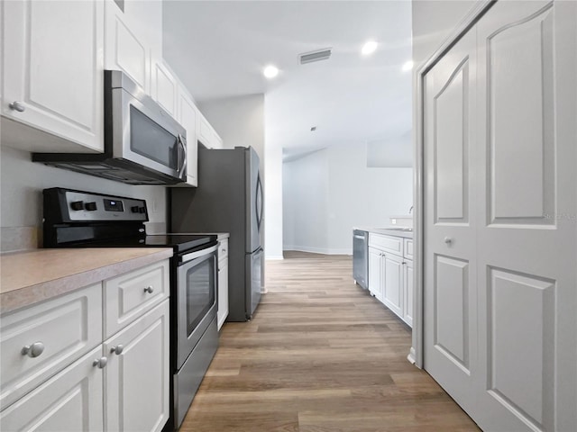 kitchen with stainless steel appliances, white cabinetry, and light hardwood / wood-style floors