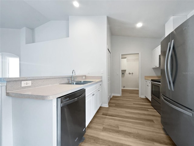 kitchen featuring kitchen peninsula, stainless steel appliances, lofted ceiling, white cabinets, and sink